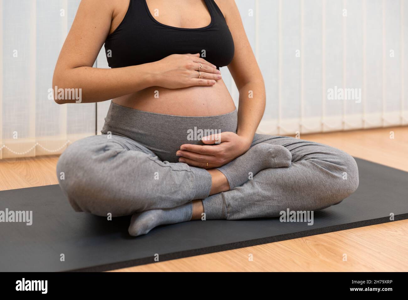 Una donna incinta rilassata seduta su un tappeto che fa yoga a toccare il suo ventre al centro benessere Foto Stock