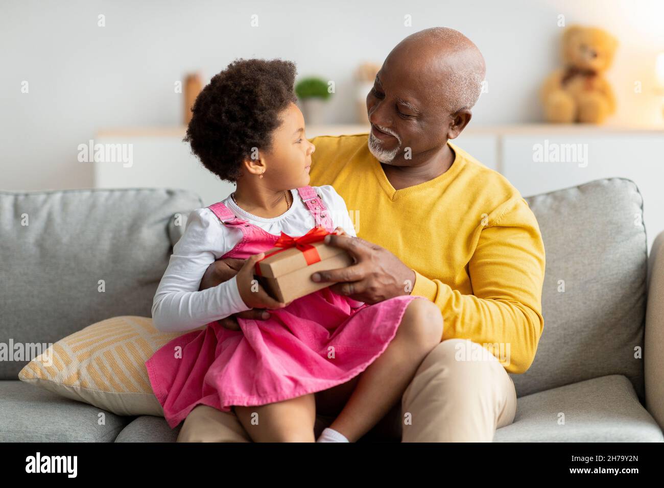 Felice african american bambina ottenere regalo di compleanno, apre scatola da uomo anziano in soggiorno interno Foto Stock