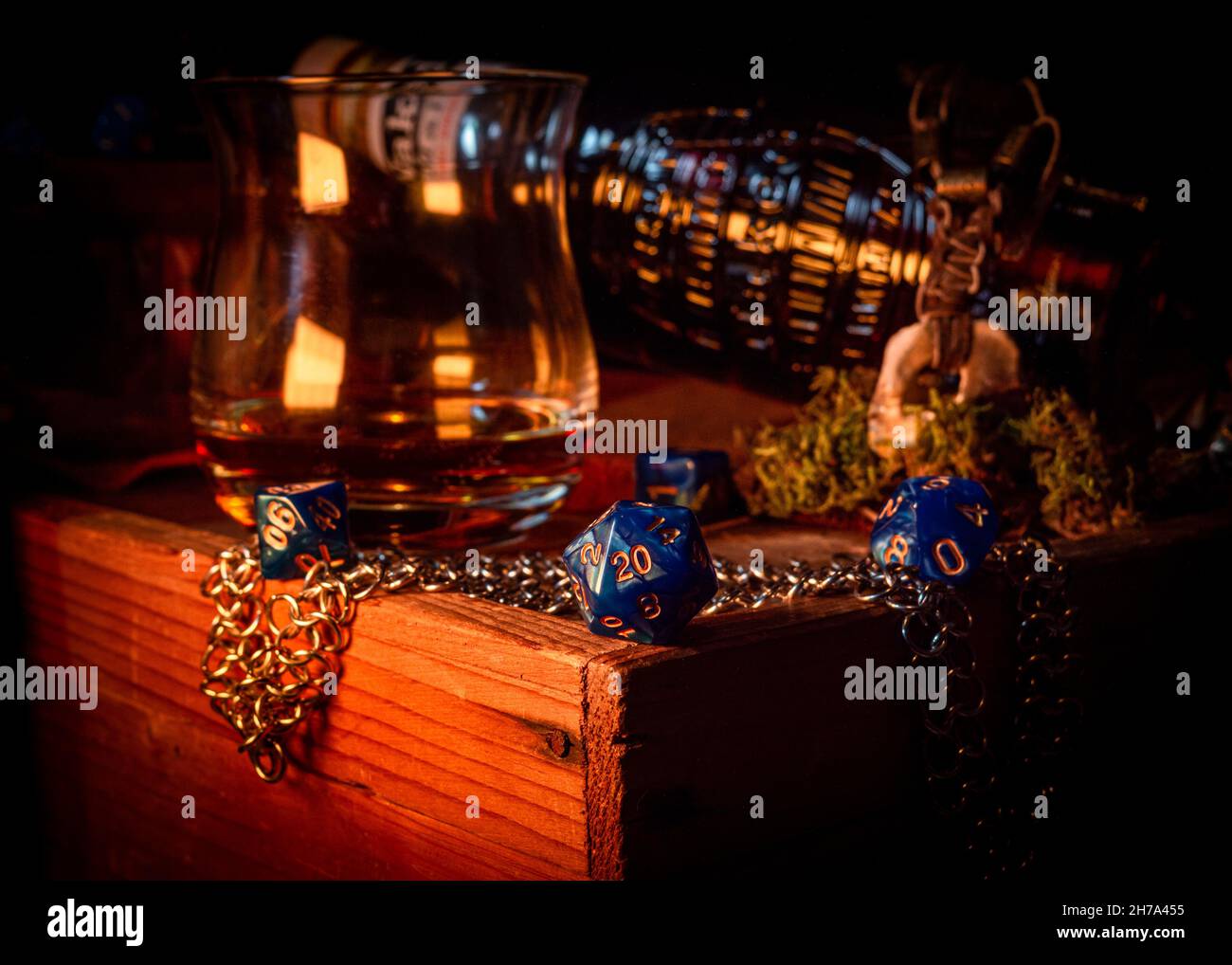 Immagine ravvicinata di un d20 blu su una scatola di legno sullo sfondo di un bicchiere di whiskey e di una bottiglia di vetro Foto Stock