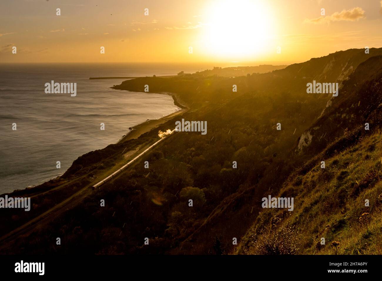 La locomotiva a vapore Clan Line corre lungo la costa a Cautle-le-ferne tra dover e Folkstone con il Belmond British Pullman sotto un arcobaleno autunnale Foto Stock