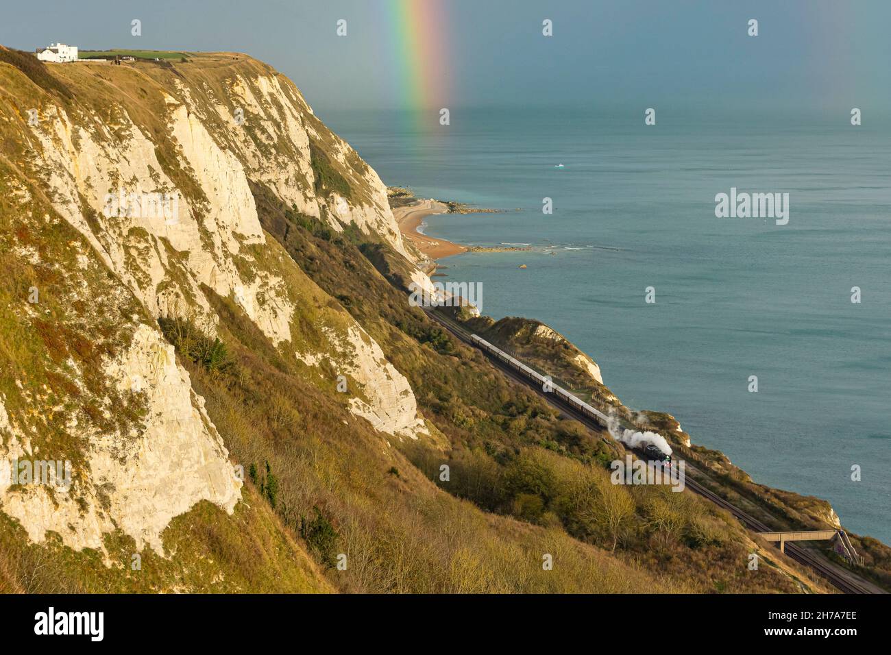 La locomotiva a vapore Clan Line corre lungo la costa a Cautle-le-ferne tra dover e Folkstone con il Belmond British Pullman sotto un arcobaleno autunnale Foto Stock