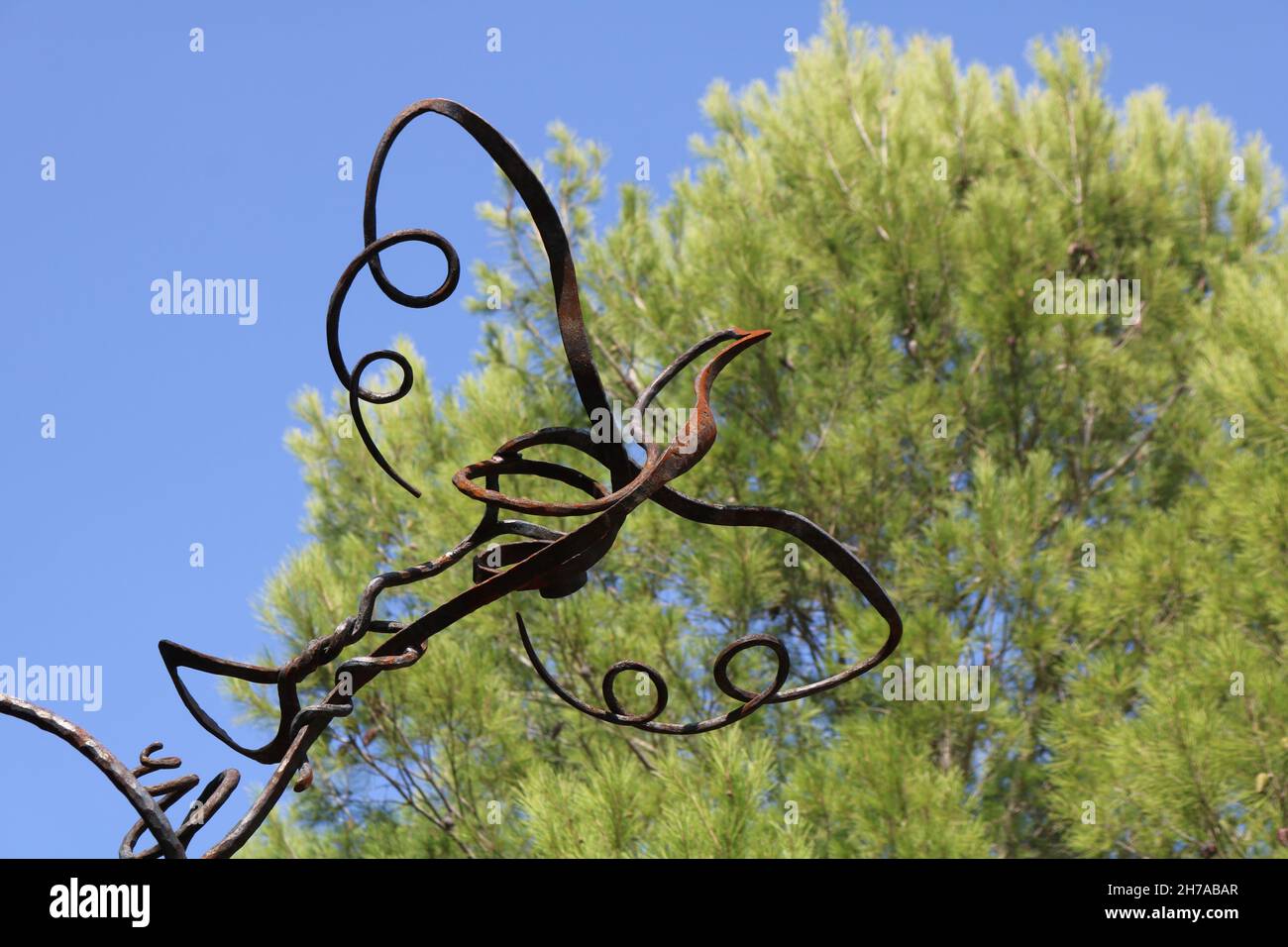 Scultura in ferro battuto di un uccello volante contro il cielo blu e un albero Foto Stock