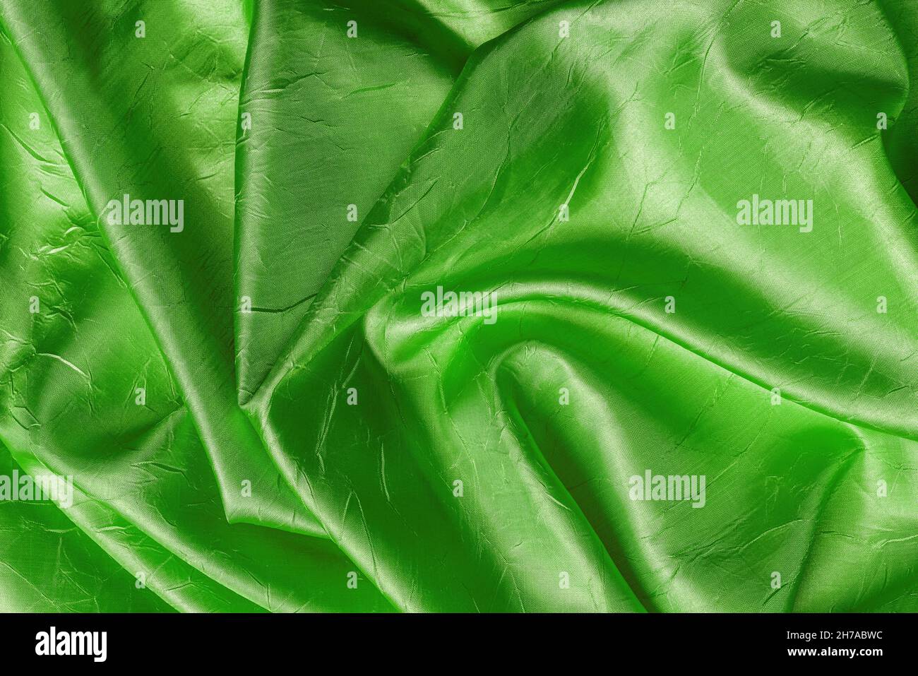 Drappeggiato di seta grinzita lucida di colore verde kelly texture. Sfondo di tessuto verde smeraldo piegato in raso. Elegante tessuto sgualcito di lusso. Foto Stock