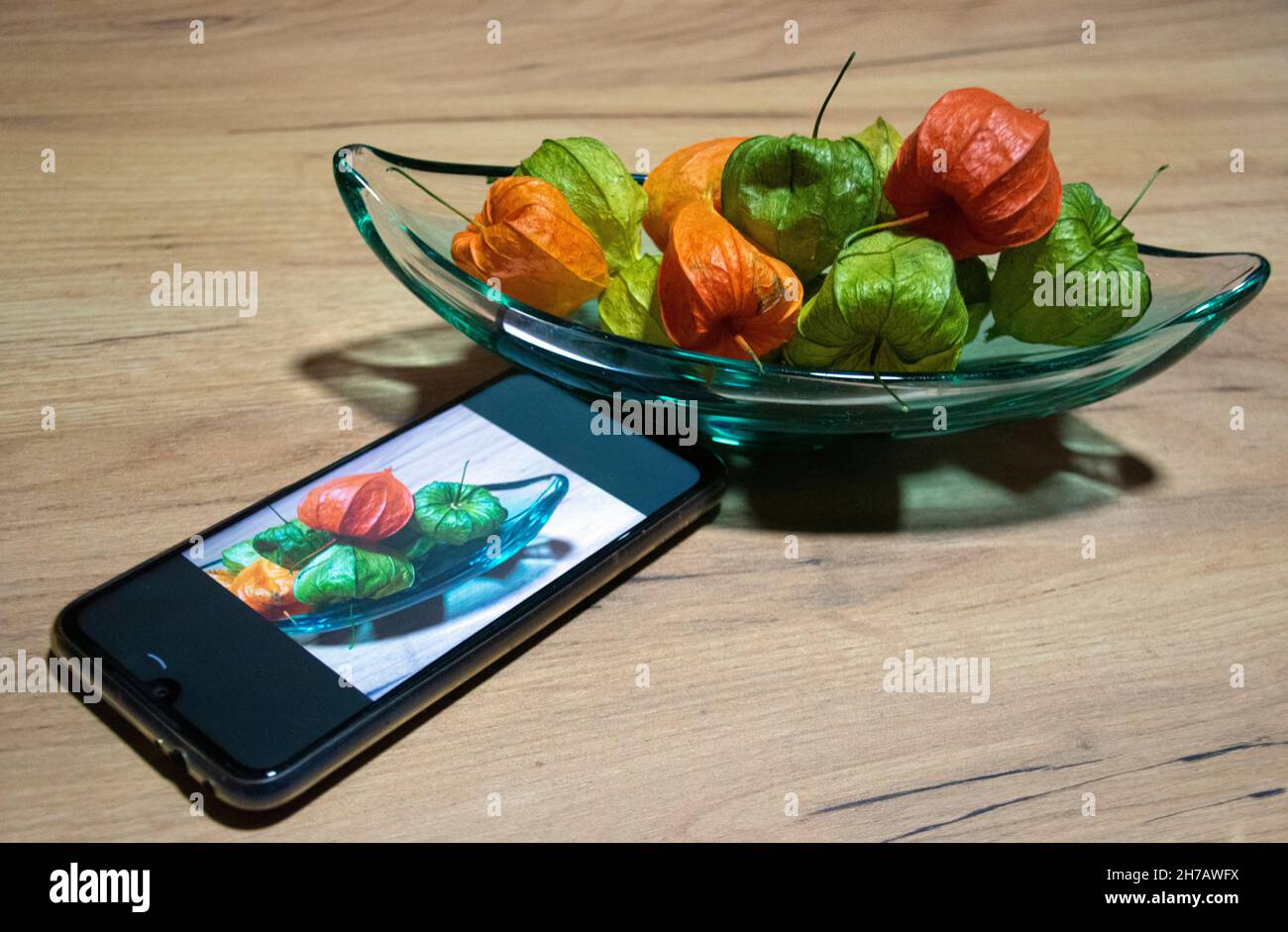 Ancora vita, una ciotola piena di fragole andine e un telefono cellulare con una foto di quella scena. Foto Stock