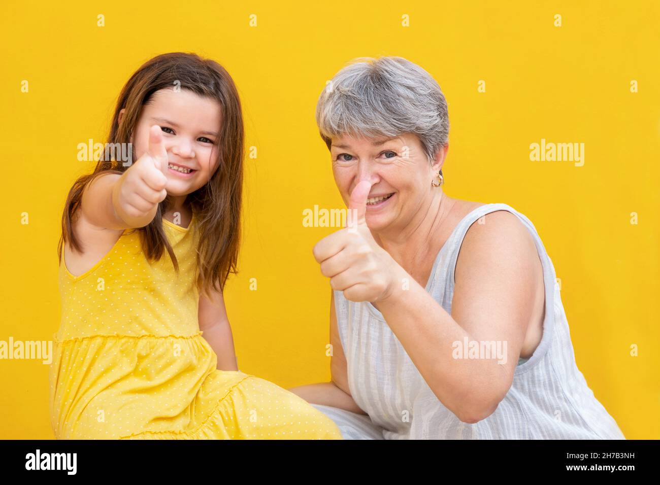 Nonna e bambino mostrano pollice su e sorriso su sfondo giallo Foto Stock