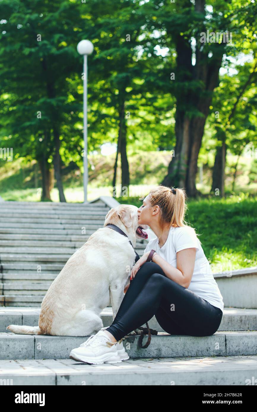 Ritratto di una donna seduta con il suo cane labrador sulle scale, baciare e abbracciare. Passeggiate mattutine. Amicizia tra uomo e cane Foto Stock