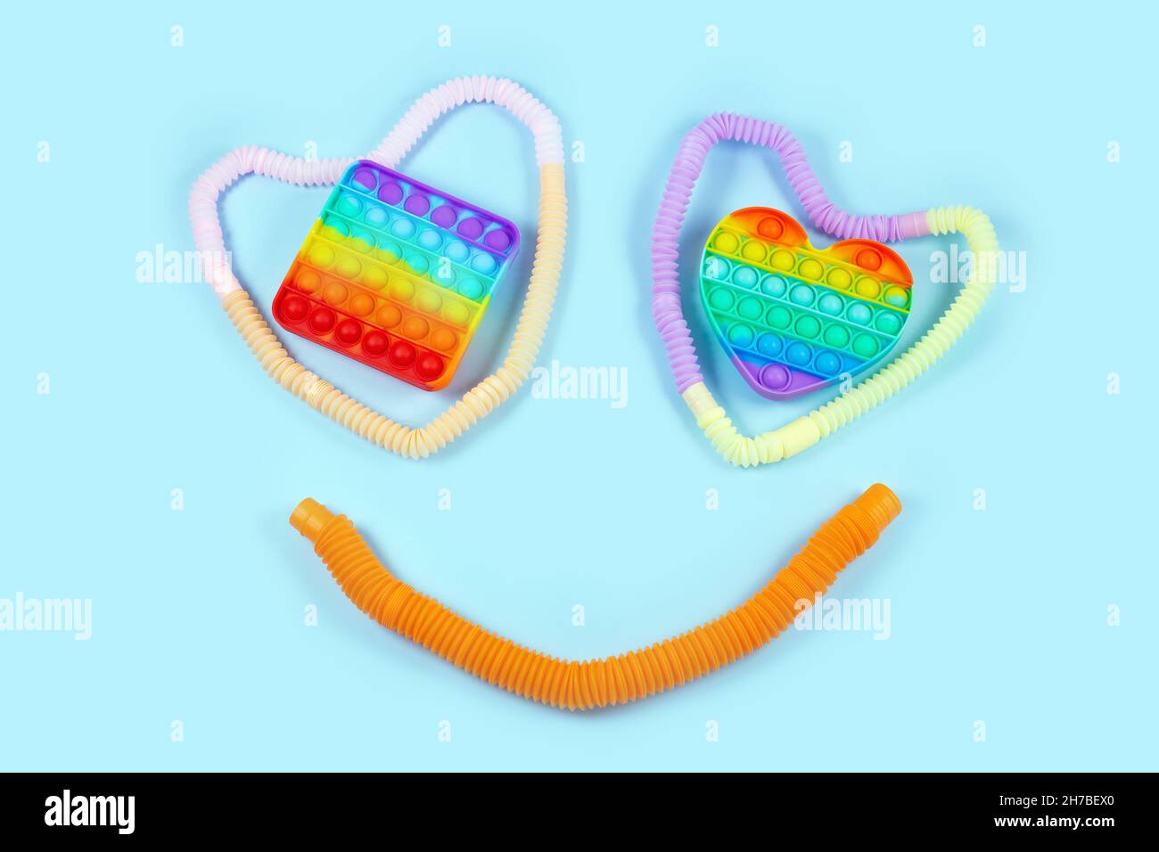 Sorridi dal tubo corrugato in plastica multicolore e schiocalo su sfondo blu. Anti-stress sensoriale figet giocattolo di tendenza in plastica del 2021. Disposizione piatta, vista dall'alto. Foto Stock