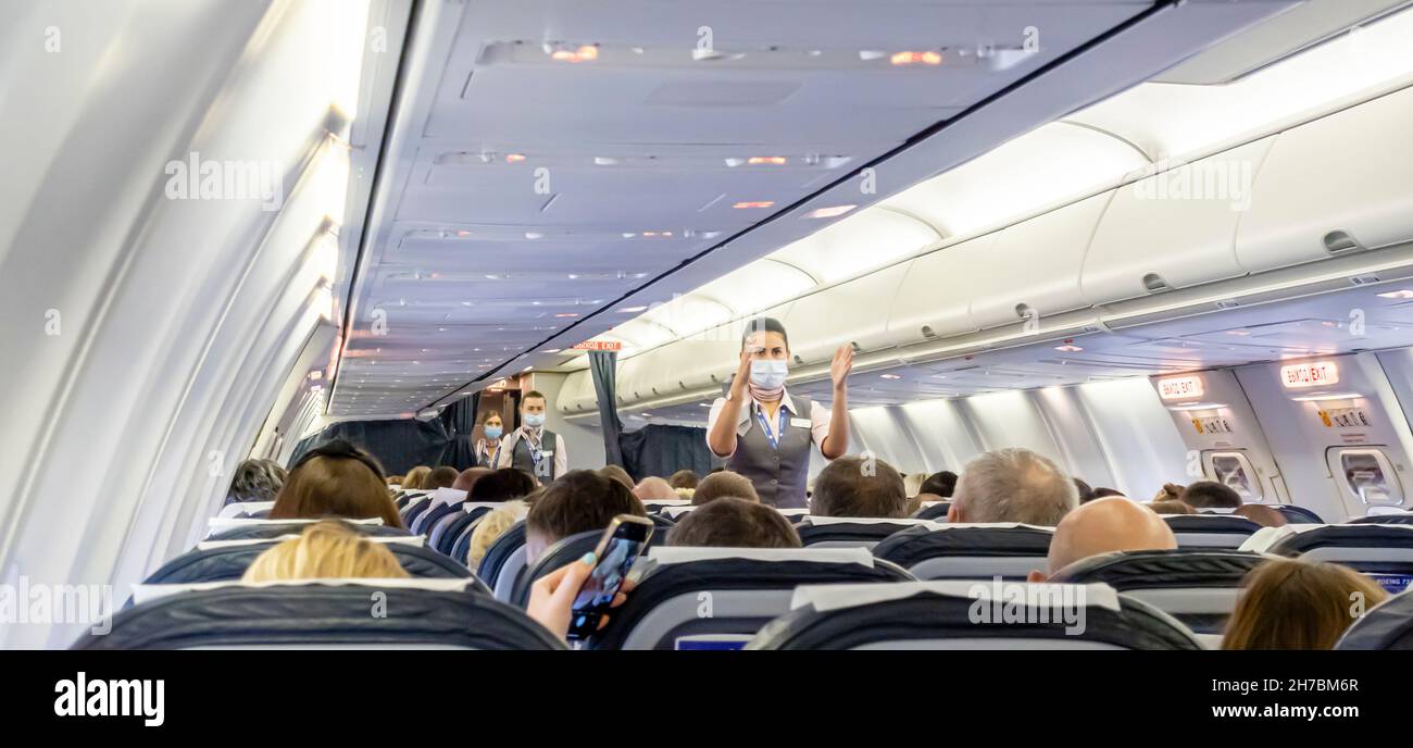 Assistente di volo femminile in maschera facciale che mostra le uscite di emergenza per i passeggeri seduti sulle sedie di un aereo Boeing 737-800 Belavia Foto Stock