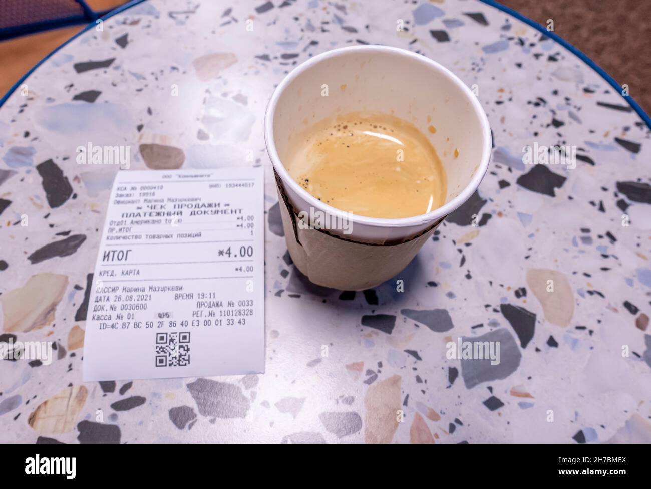 Cafe americano in una tazza di carta con carta da imballaggio su un tavolo con ricevuta di acquisto per un totale di 4 BYN ($1.59) Foto Stock
