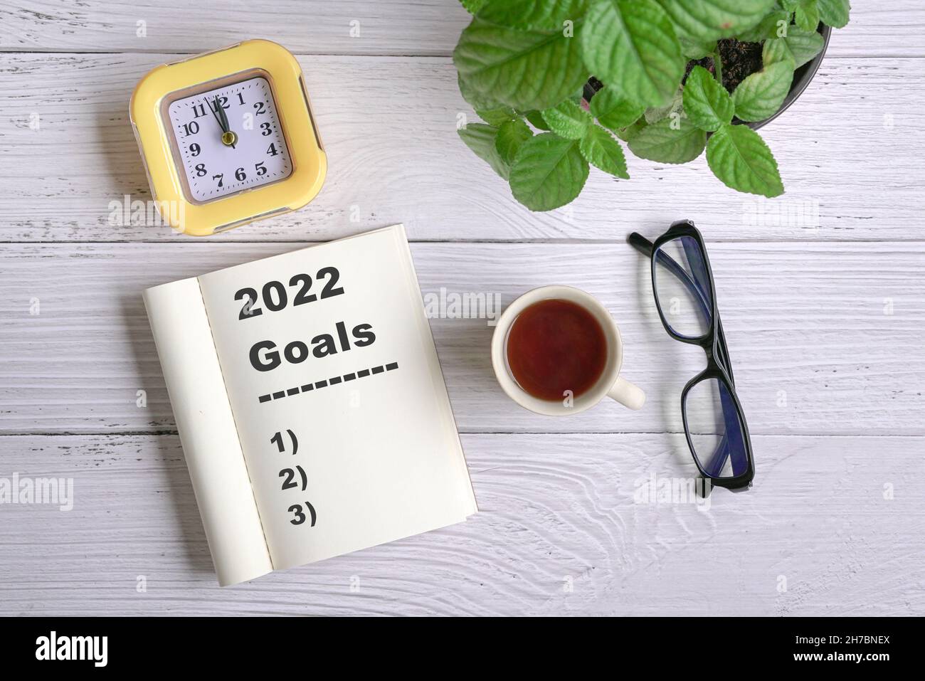 Gli obiettivi di nuovo anno 2022 su scrivania. Vista dall'alto con caffè, blocco note, orologio, occhiali e piante verdi. Foto Stock
