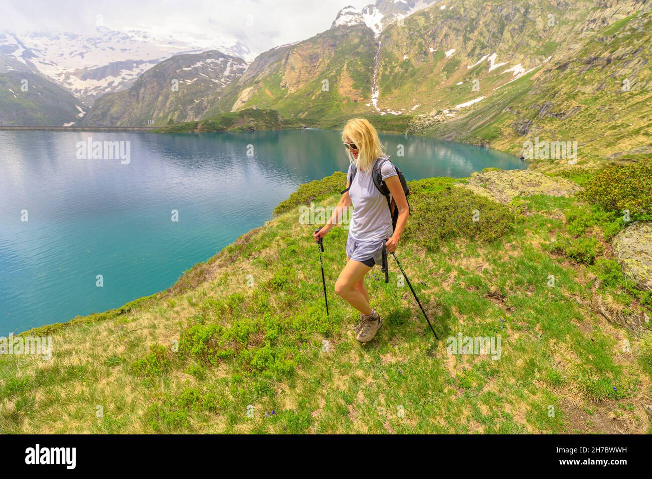 backpacker donna turistica trekking con poli sul lungolago del lago Robiei e la sua diga. Serbatoio svizzero nel Cantone della Maggia Valle del Ticino. Parte superiore di Foto Stock