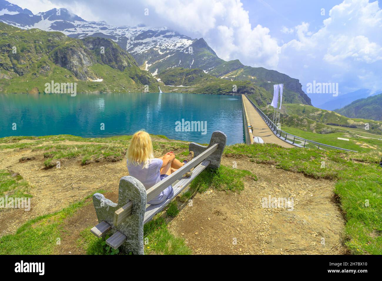 Vista aerea sulla diga di Robiei in Svizzera: ragazza backpacker dopo il trekking, poggiato su una panchina del lago Robiei. Riserva svizzera in Valle Maggia Foto Stock