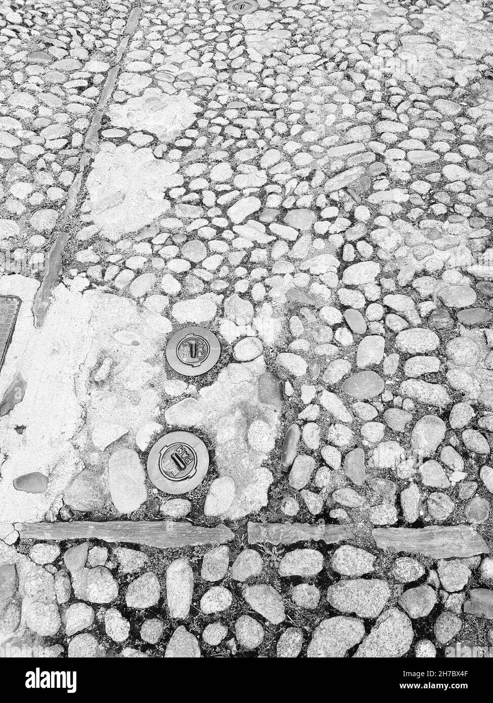 Dettaglio bianco e nero della vecchia strada con ciottoli e due idranti a corte, Corsica, Francia Foto Stock