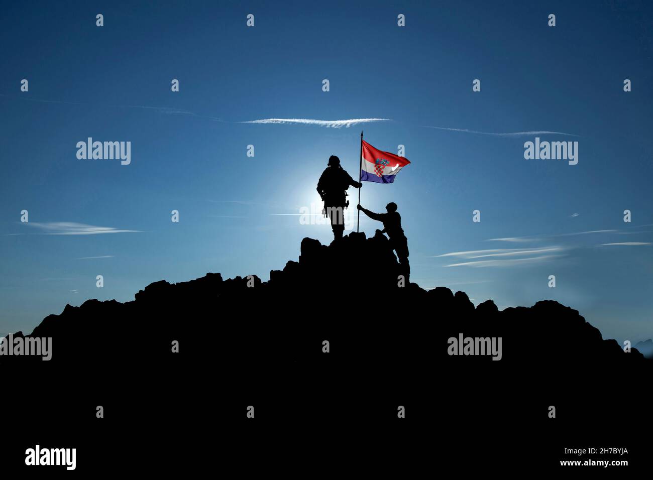 Due soldati irriconoscibili innalzano la bandiera croata sulla cima di una montagna Foto Stock