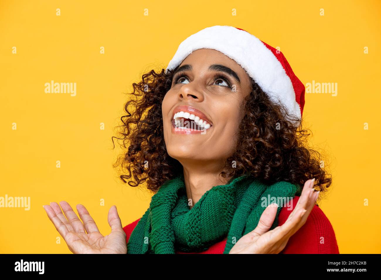 Primo piano ritratto di eccitata giovane bella afroamericana donna in abbigliamento di Natale sorridente e guardando verso l'alto su isolato studio giallo backgroun Foto Stock