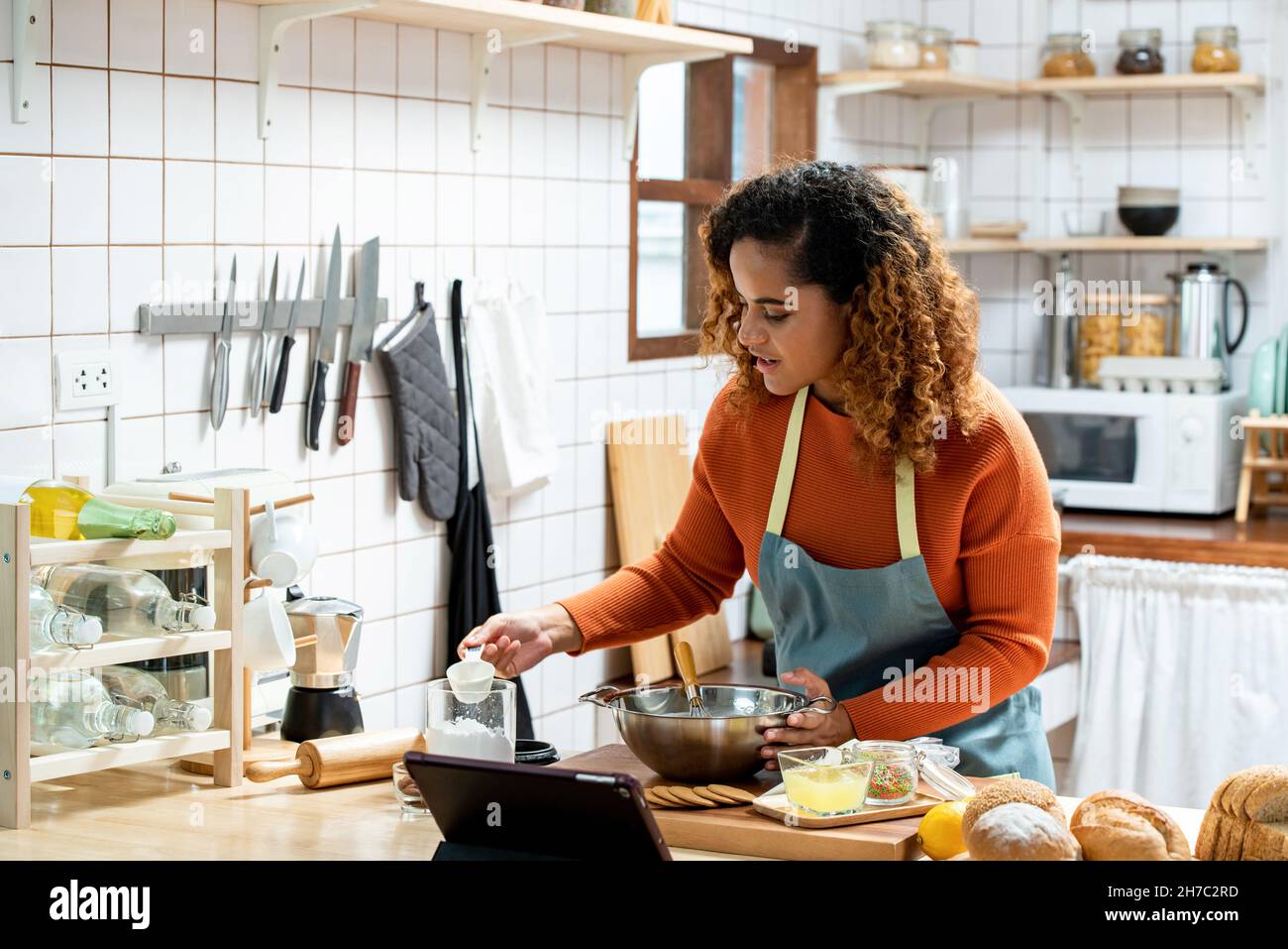 Giovane bella donna afroamericana in cucina imparando online lezione di cucina virtuale da tablet computer a casa Foto Stock
