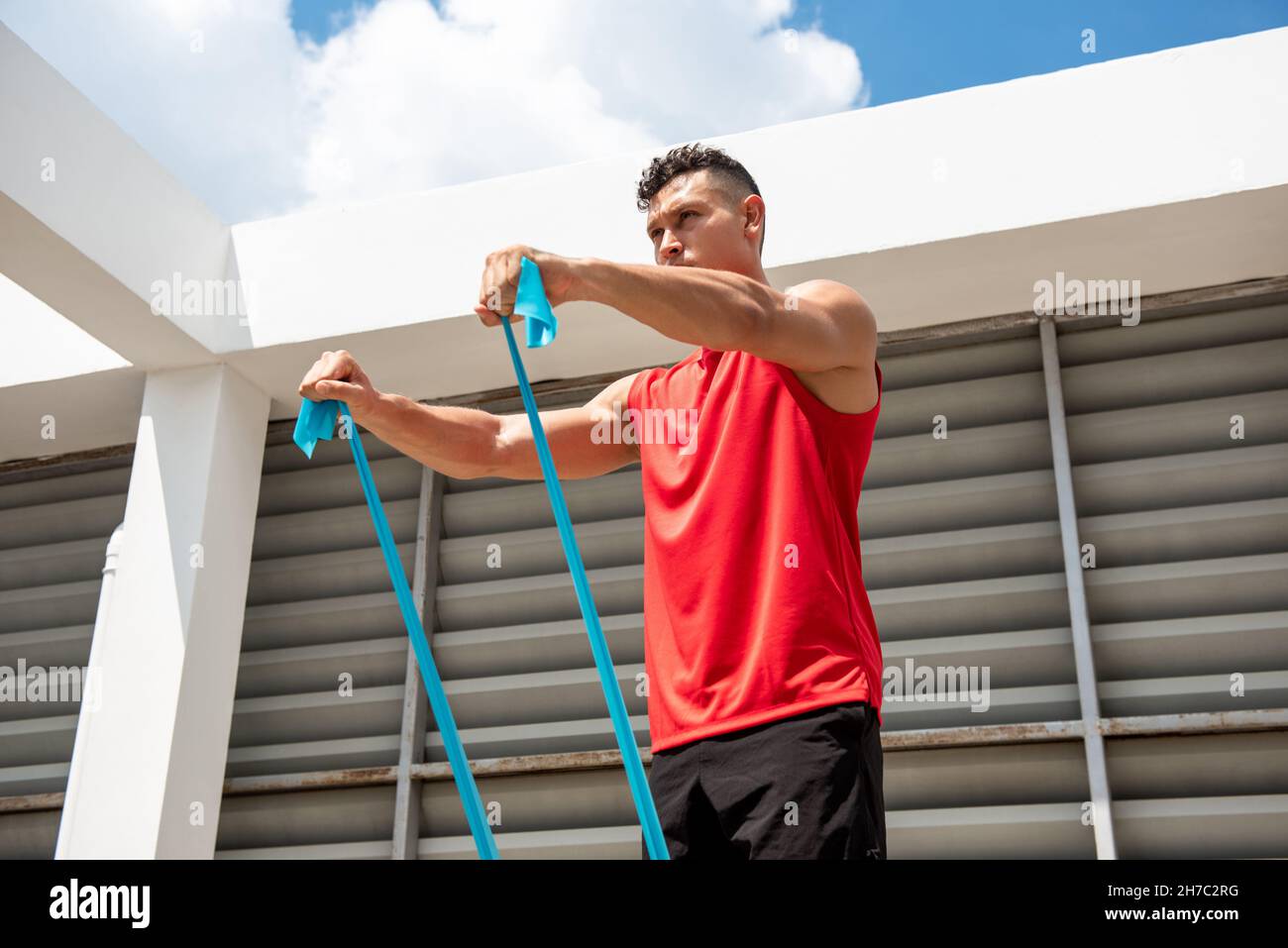 Ritratto di fit muscolare uomo sportivo facendo esercizio spalla anteriore con fascia di resistenza sul tetto della costruzione Foto Stock