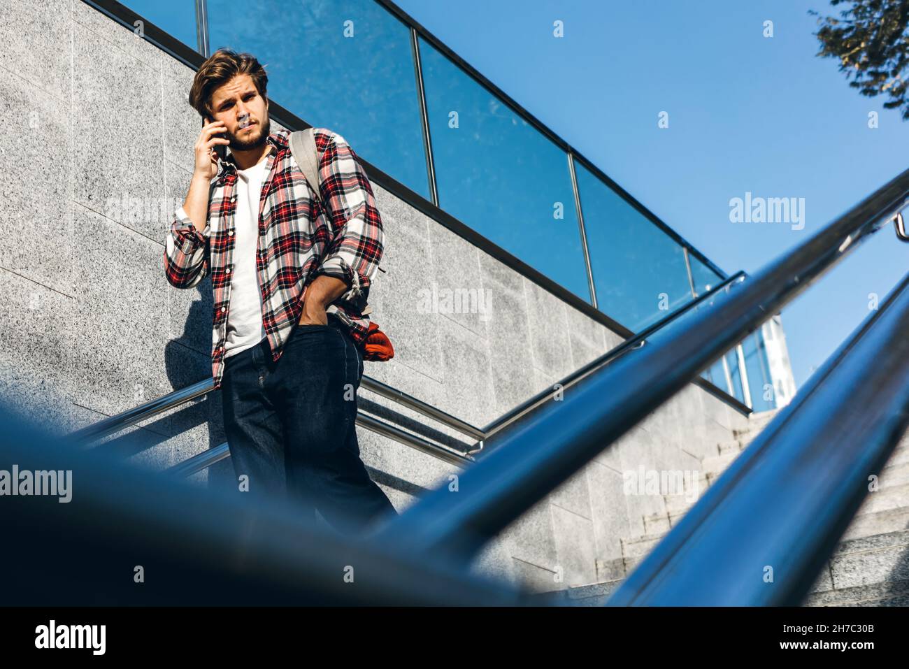 Ritratto di giovane moderno bello che parla al telefono. Hipster ragazzo con mobile in mano all'aperto. Scale urbane, strada della città Foto Stock