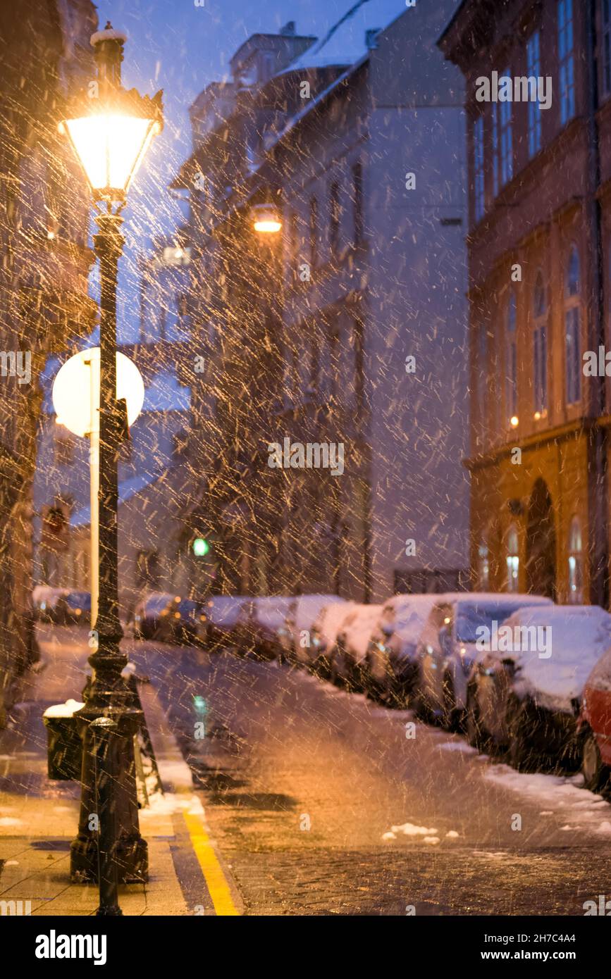 Fiocchi di neve che volano sotto la lampada stradale nella strada della città vecchia Foto Stock