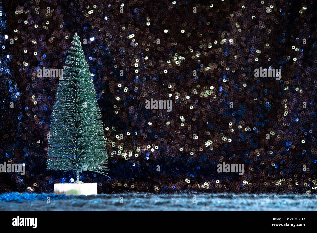 Mini albero di Natale con glitter verde su paillettes blu e sfondo maglione a maglia blu teale. Stella cielo magico vacanza foresta lascape Foto Stock