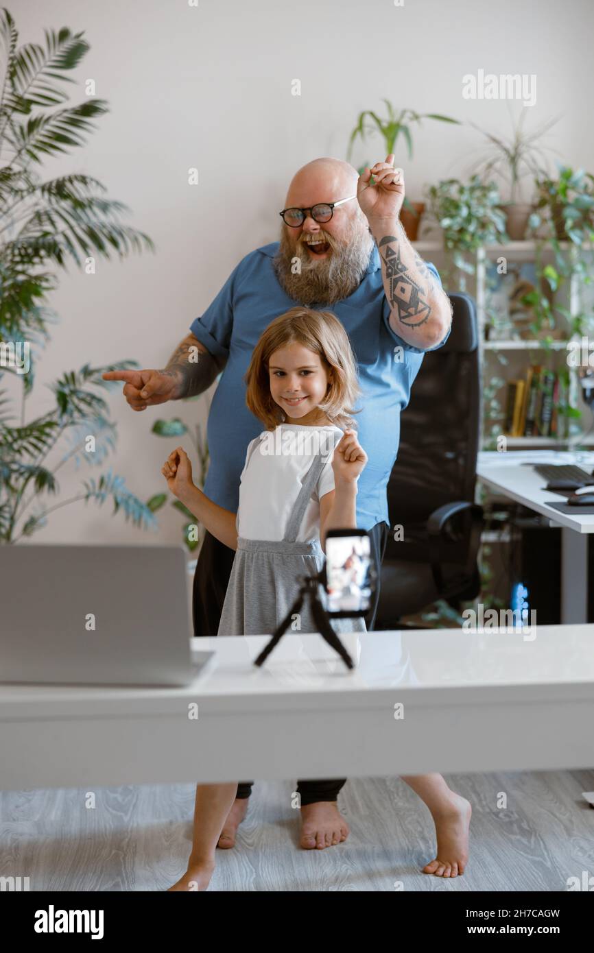 Ragazza positiva con divertente danza padre insieme registrazione nuovo video per il blog a casa Foto Stock