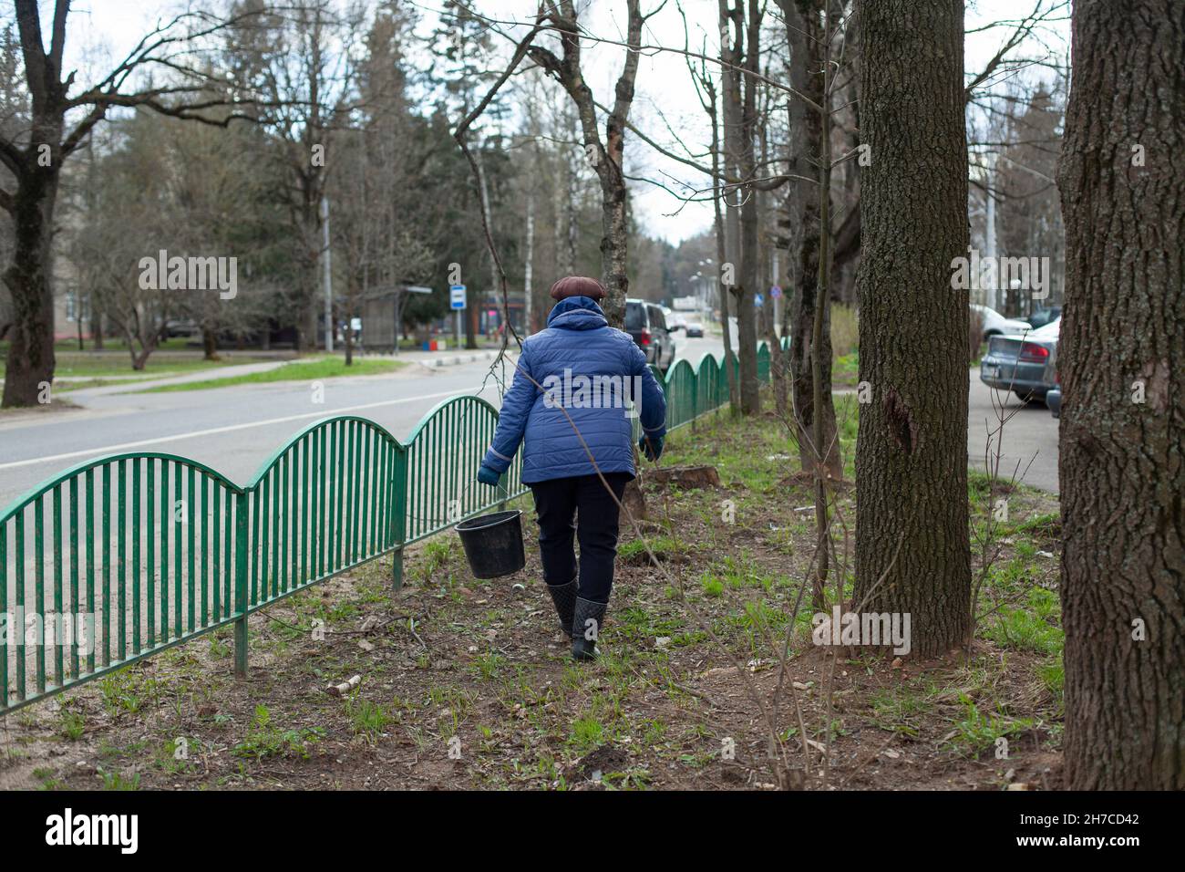 Una donna porta un secchio. Architettura paesaggistica del cantiere a Mosca. Secchio d'acqua per innaffiare piante. La donna tiene un peso in mano. Foto Stock