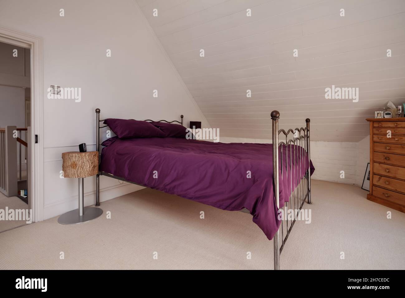 Stradeshall, Suffolk, Inghilterra - 16 giugno 2020: Camera da letto mansardata in stile loft con pareti dipinte di bianco, struttura in metallo e biancheria da letto viola Foto Stock