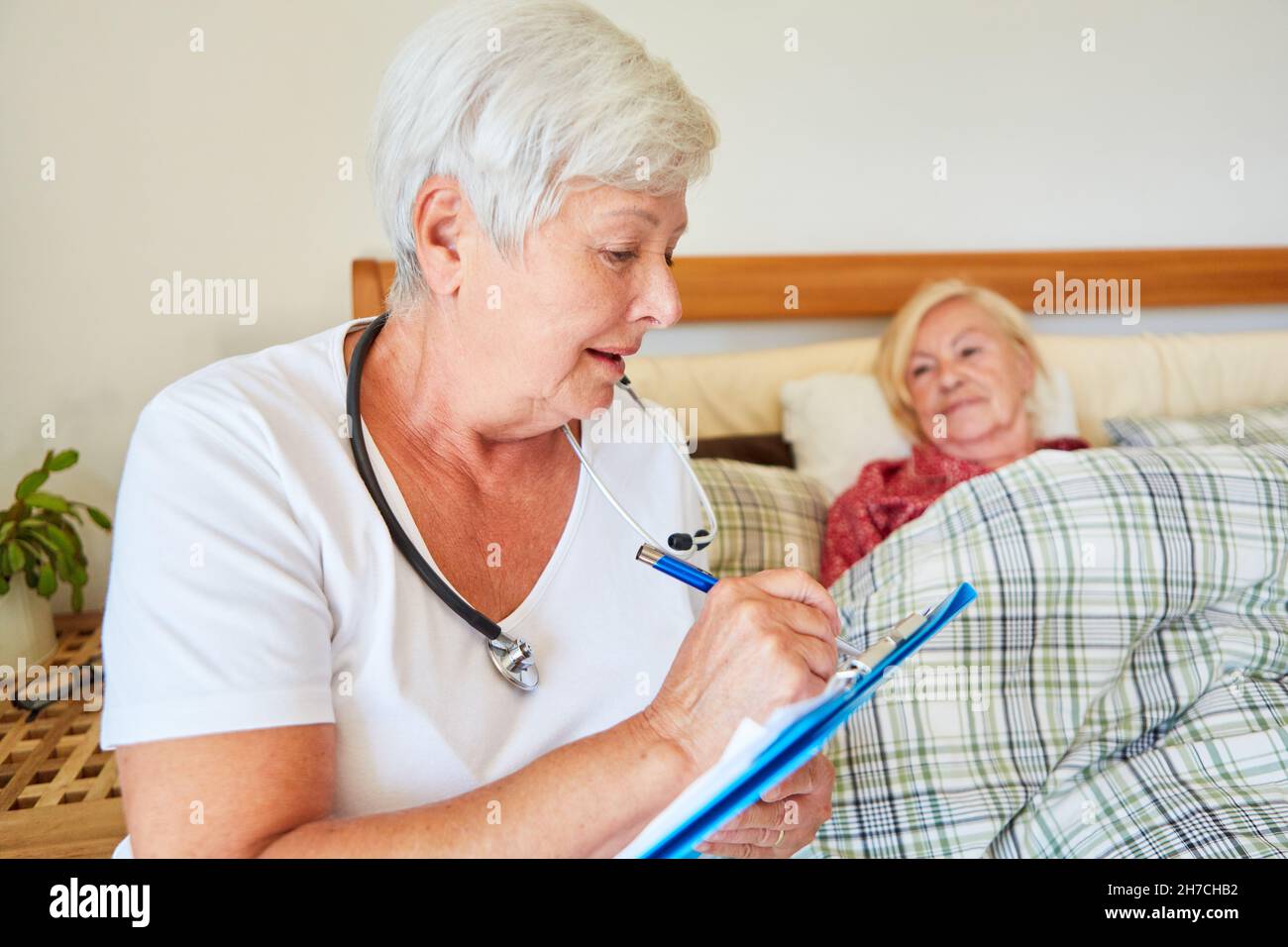 Medico con i documenti del paziente durante una chiamata di casa sul letto di un anziano nel paese o nella casa della gente anziana Foto Stock