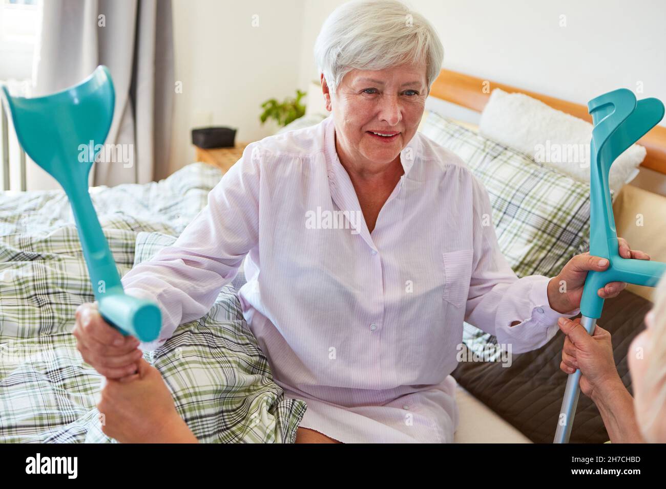Donna anziana sorridente a letto come paziente con stampelle che sono curate da infermieri geriatrici nella casa di riposo Foto Stock
