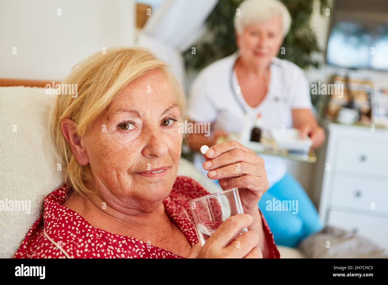 La donna anziana malata prende una tavoletta con acqua a casa curata dal personale infermieristico Foto Stock