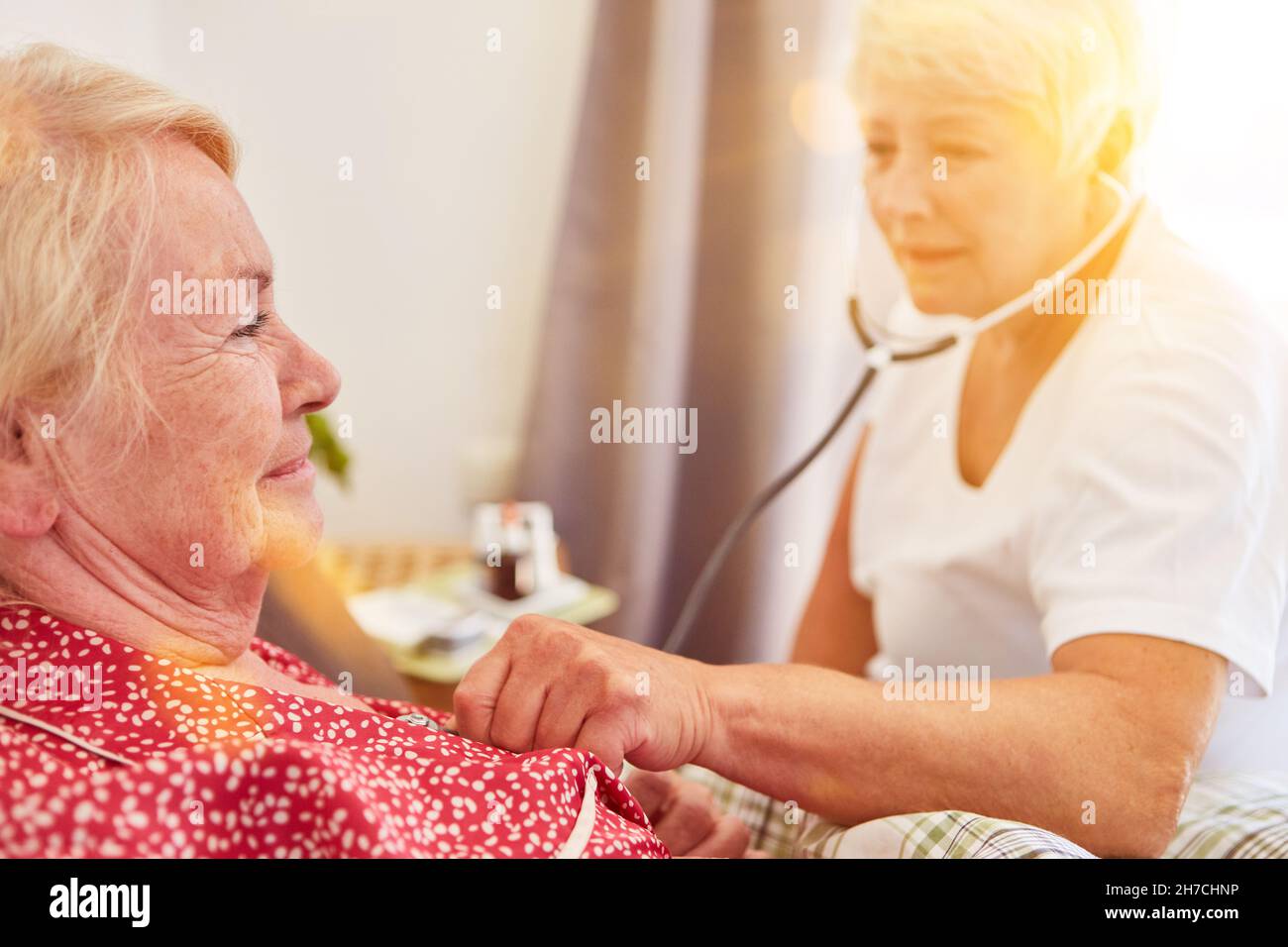 Infermiera anziana che ascolta i polmoni con stetoscopio a casa degli anziani Foto Stock