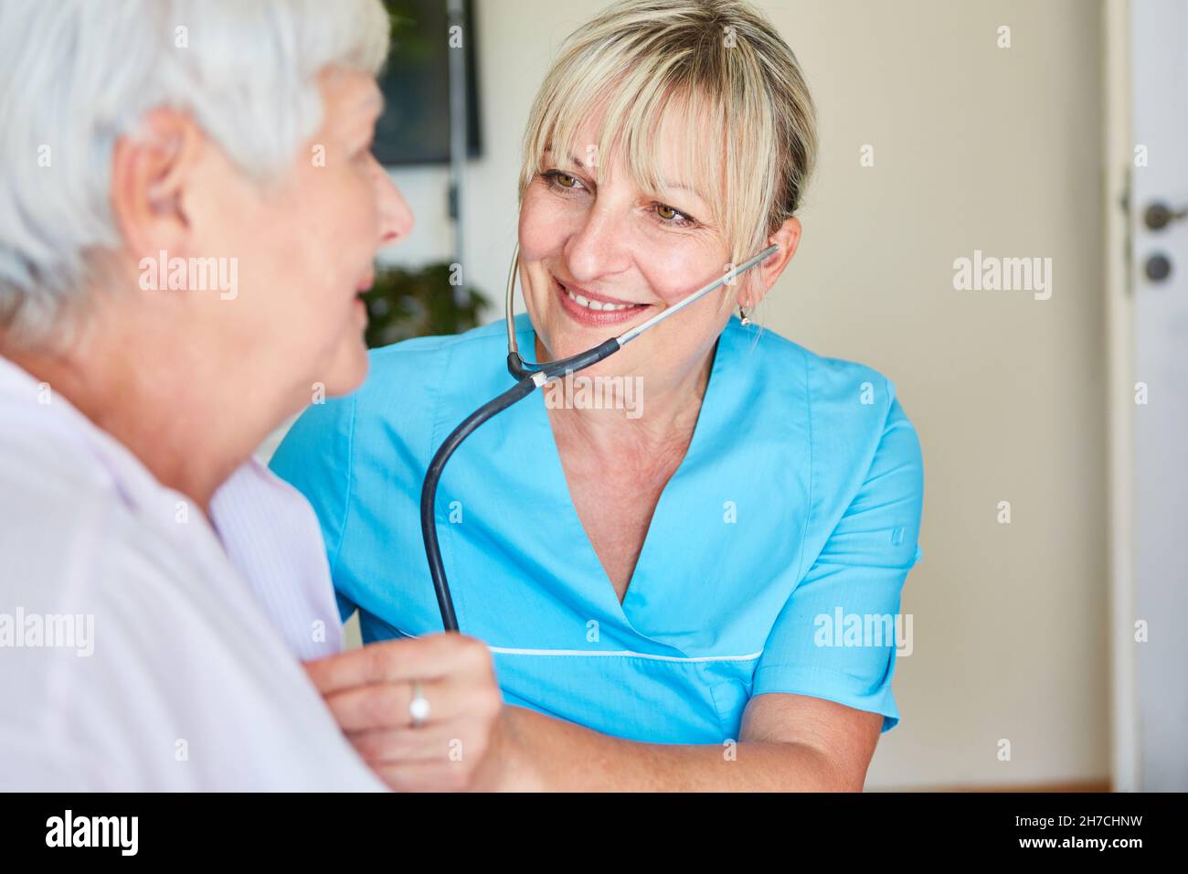 Medico femminile con stetoscopio che esamina una donna anziana su una chiamata domestica o in una casa di cura Foto Stock