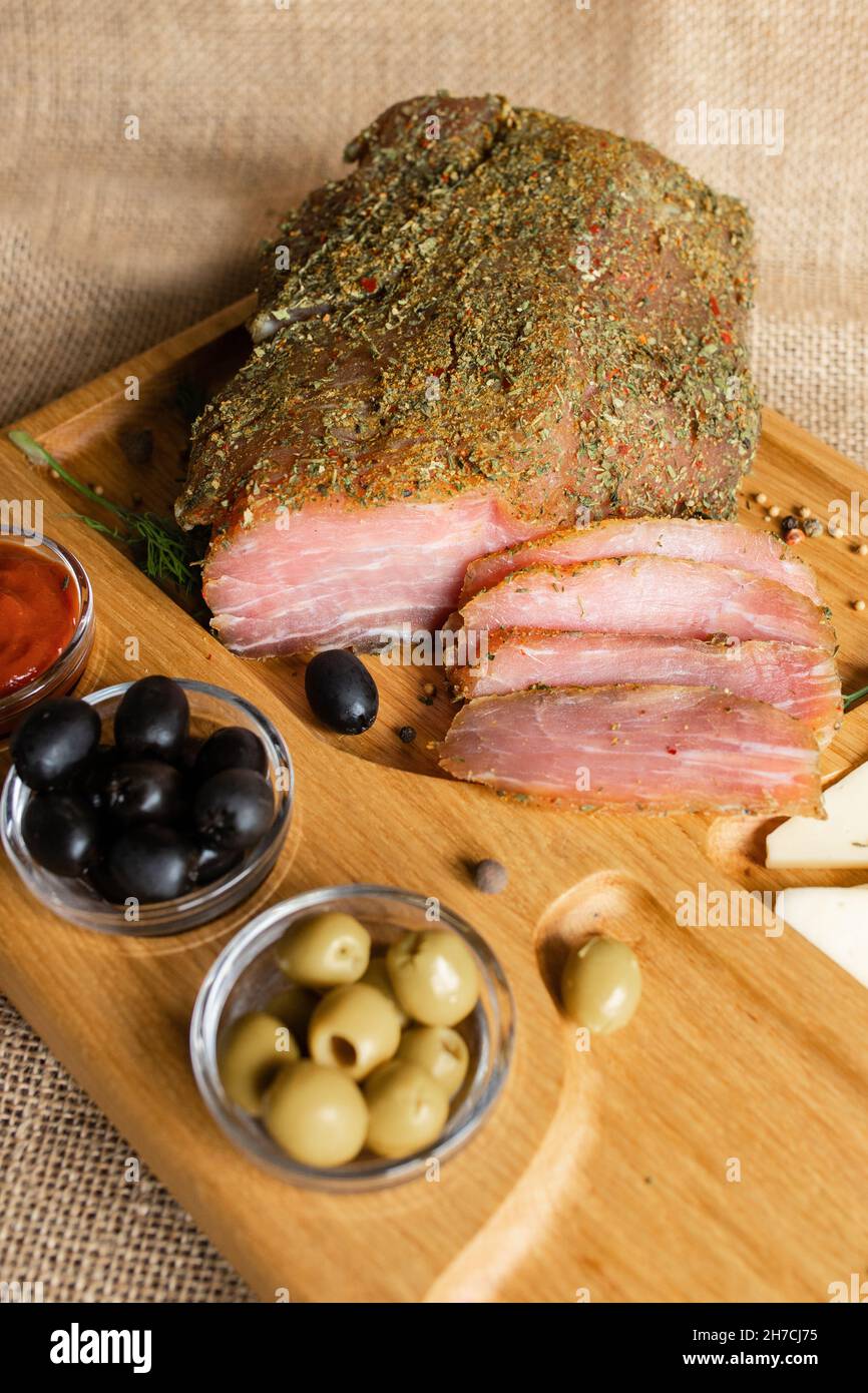 Filetto di maiale stagionato sul banco di servizio in legno con formaggio, olive, pepe nero, salsa di pomodoro. Antipasto con filetto a scatto. Piatto di bielorusso Foto Stock