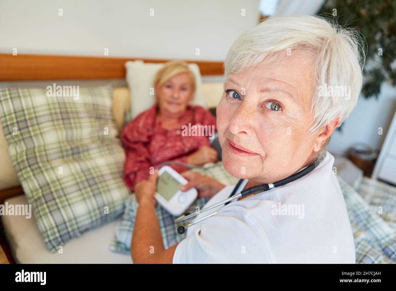 Infermiere con monitor della pressione sanguigna che misura la pressione sanguigna della donna anziana a casa Foto Stock