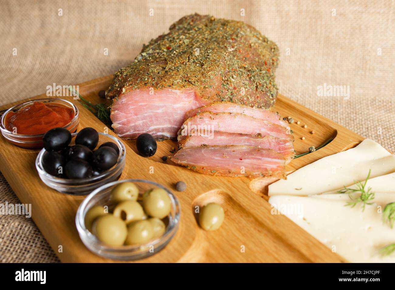 Filetto di maiale stagionato sul banco di servizio in legno con formaggio, olive, pepe nero, salsa di pomodoro. Antipasto con filetto a scatto. Piatto di bielorusso Foto Stock