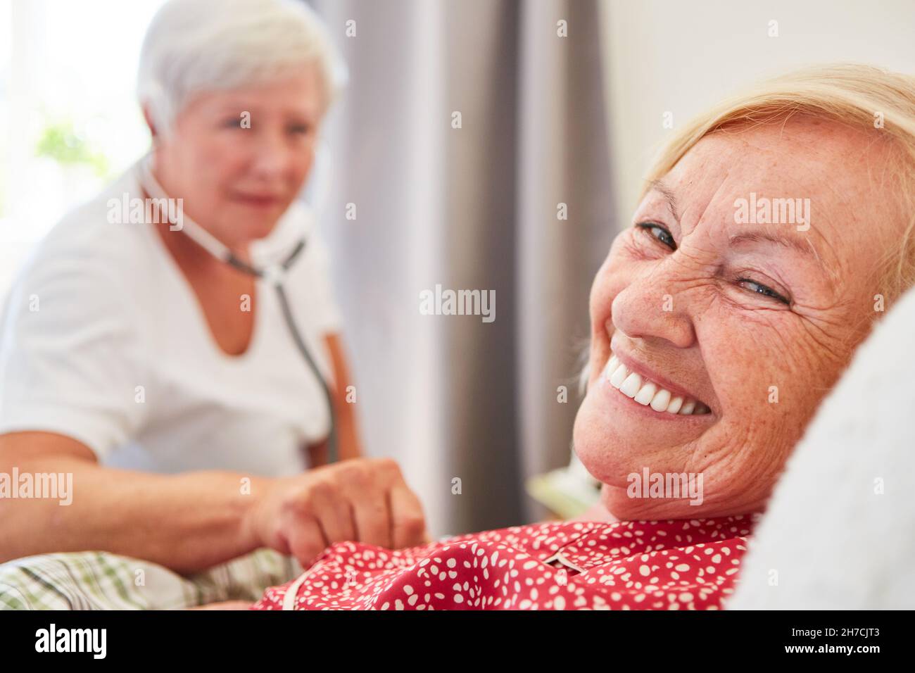 Donna anziana felice come paziente a letto è esaminato da un medico con uno stetoscopio Foto Stock