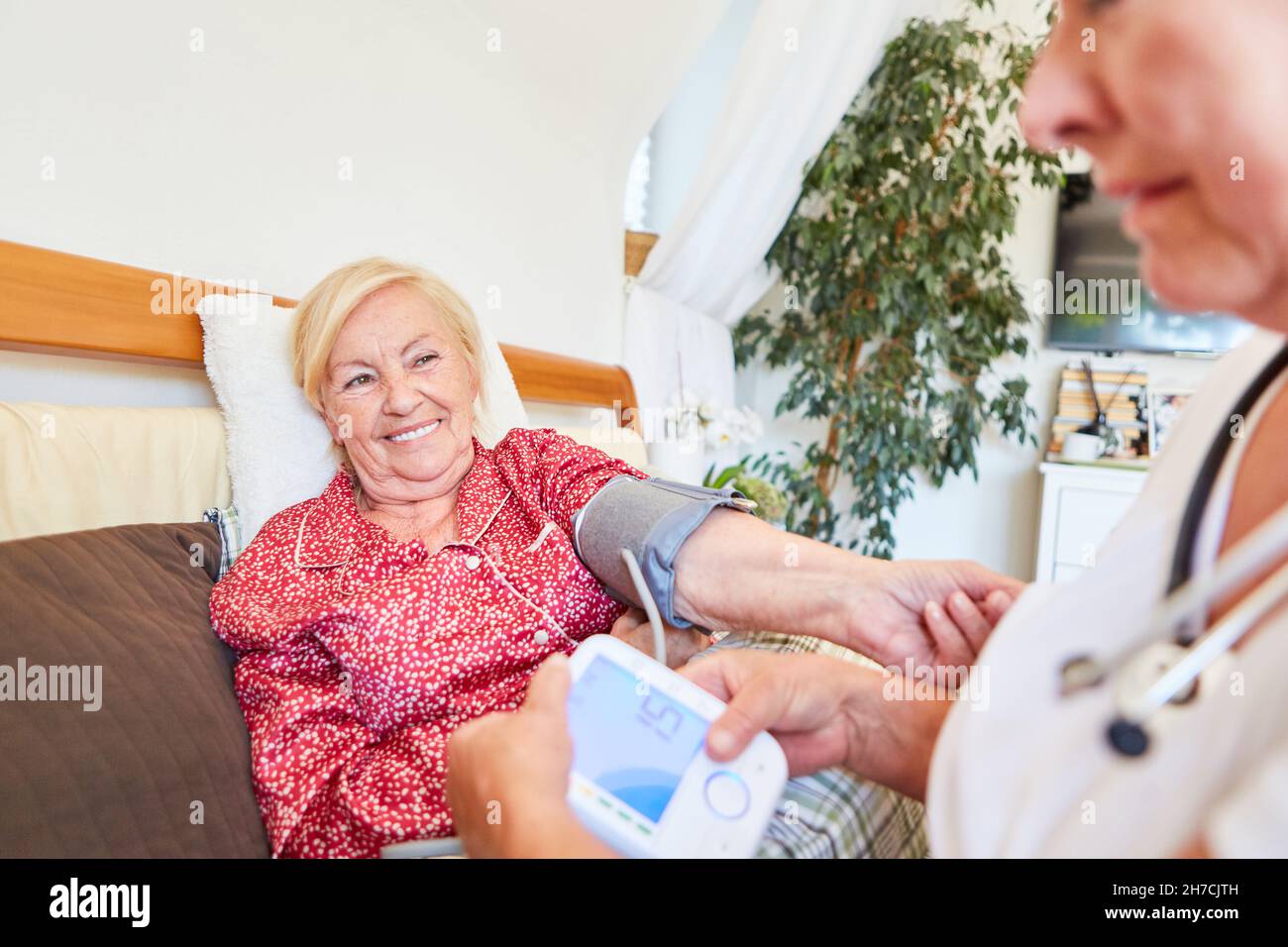 Donna che allatta o infermiera geriatrica che prende le misurazioni della pressione sanguigna a casa o in una casa di cura Foto Stock