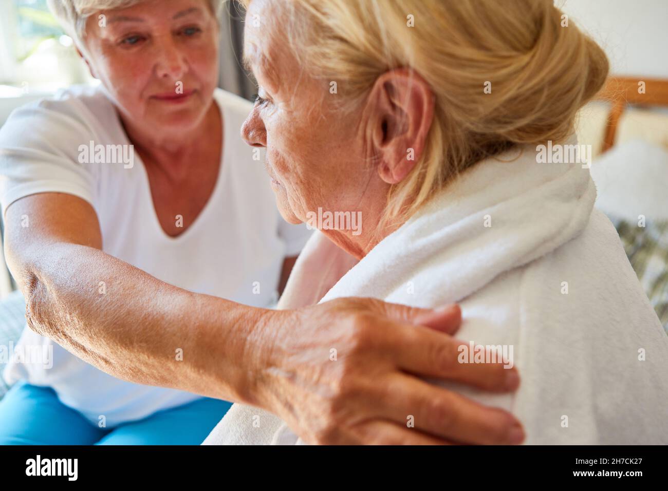 Una donna del servizio infermieristico si prende cura di una donna anziana in un accappatoio a casa Foto Stock