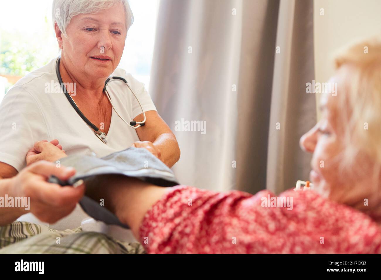 Un'infermiera geriatrica o un medico che misura la pressione sanguigna degli anziani a casa o a casa di un anziano Foto Stock