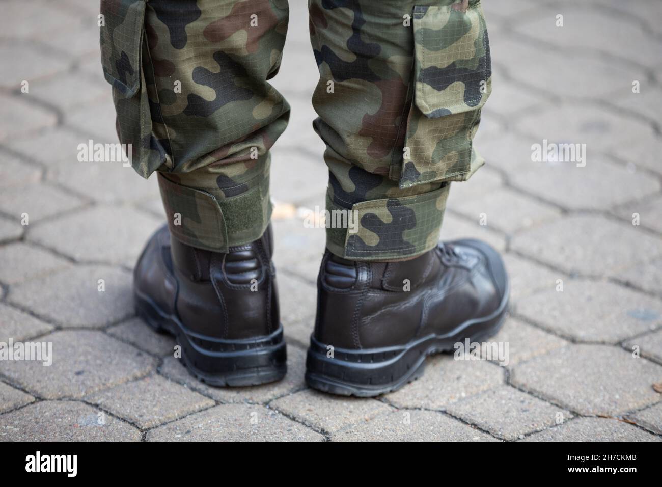 Un uomo militare vestito di pantaloni moro e stivali in pelle si erge su un ciottolato. Foto Stock