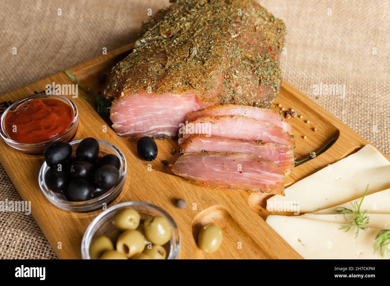 Filetto di maiale stagionato sul banco di servizio in legno con formaggio, olive, pepe nero, salsa di pomodoro. Antipasto con filetto a scatto. Piatto di bielorusso Foto Stock