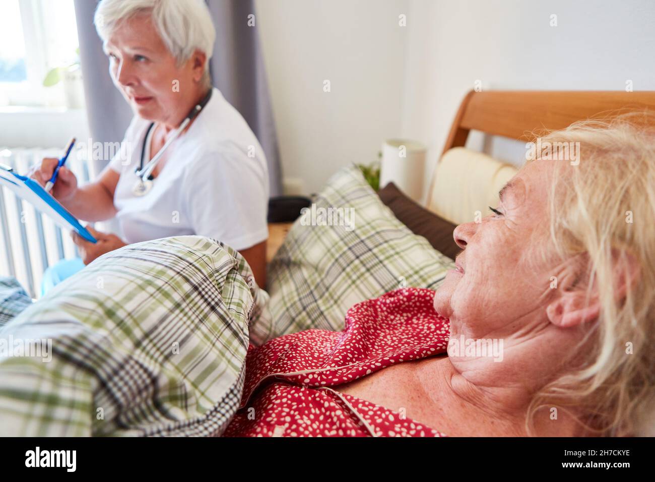 Anziani come paziente a letto e un medico con cartelle paziente durante una visita a casa nella casa di cura Foto Stock
