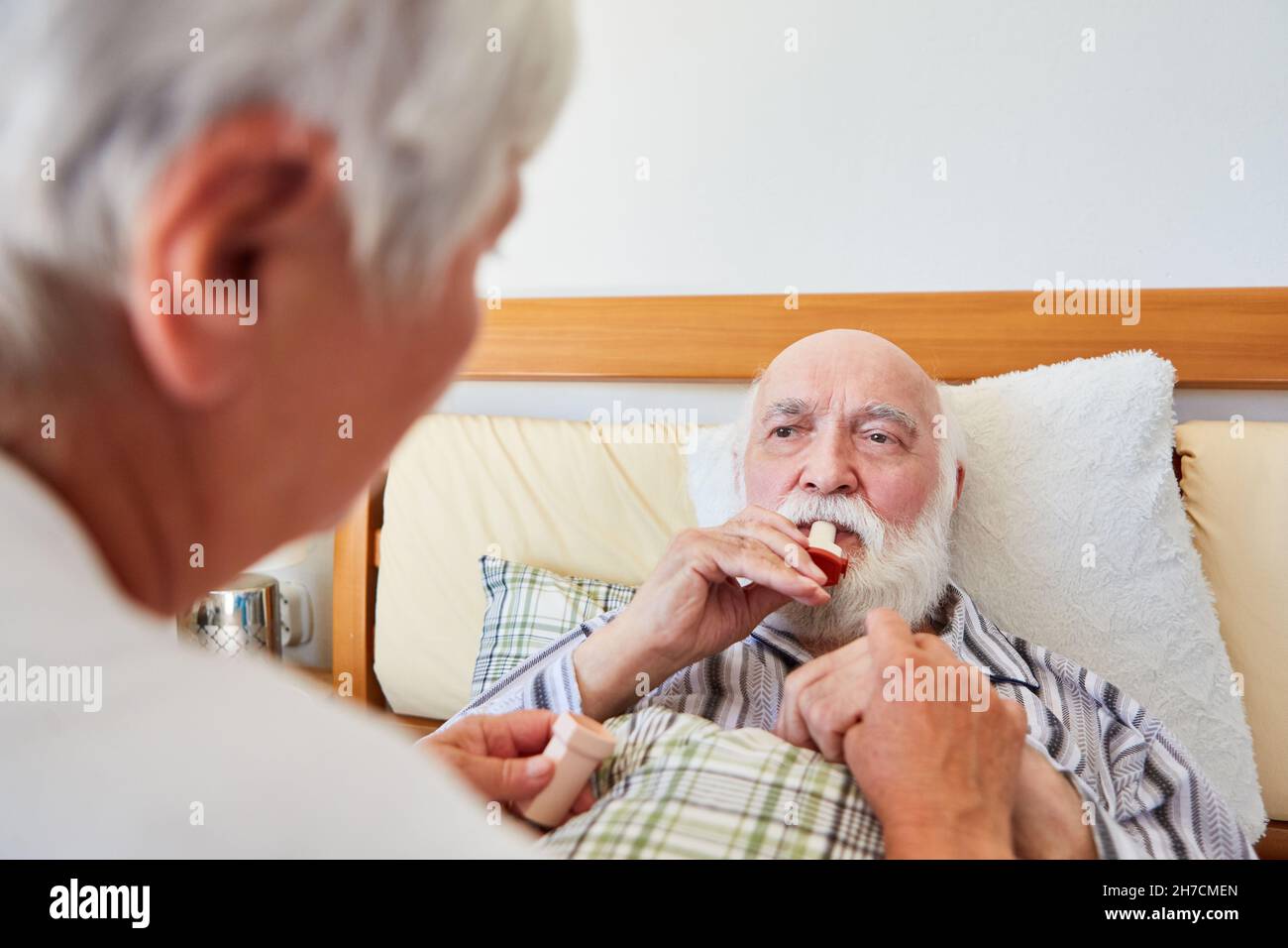 Senior in letto d'ospedale utilizza l'asma spray con l'assistenza di un infermiere geriatrico Foto Stock