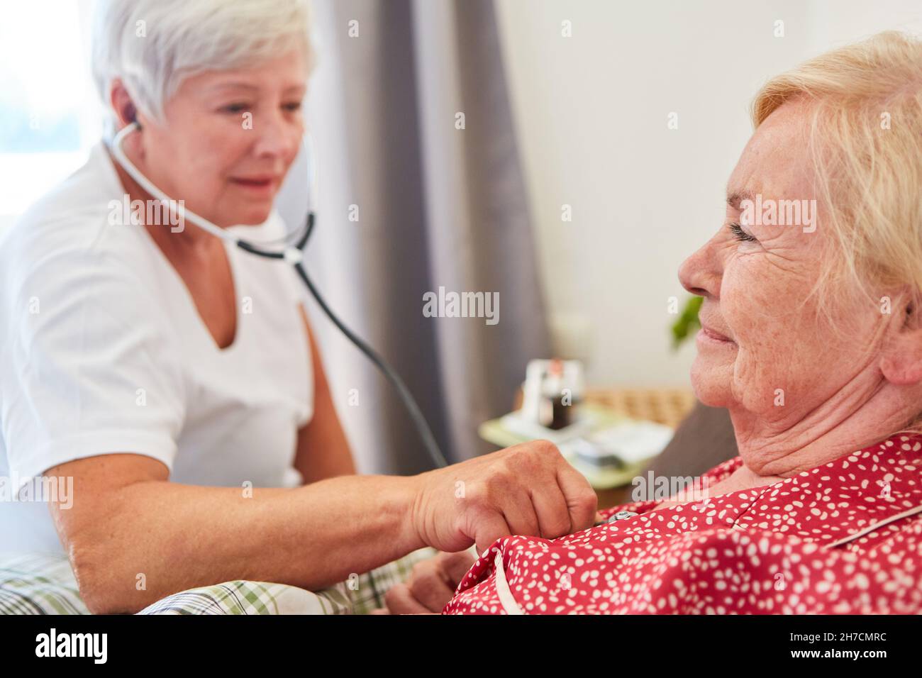 Casa di cura per anziani anziane donna a casa mentre ascoltano stetoscopio Foto Stock