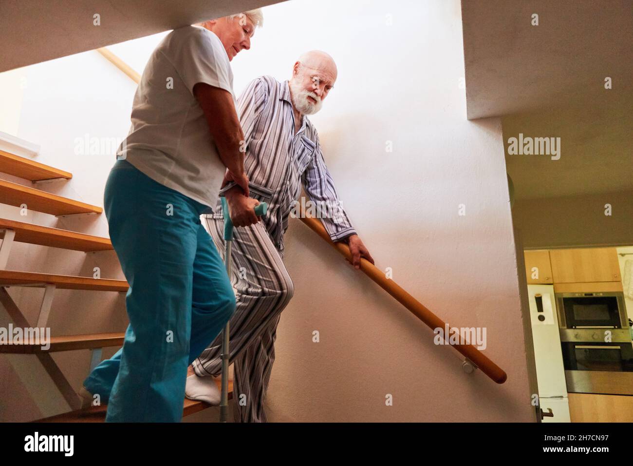 L'infermiera geriatrica sostiene gli anziani con le stampelle quando salite le scale nelle cure domestiche Foto Stock