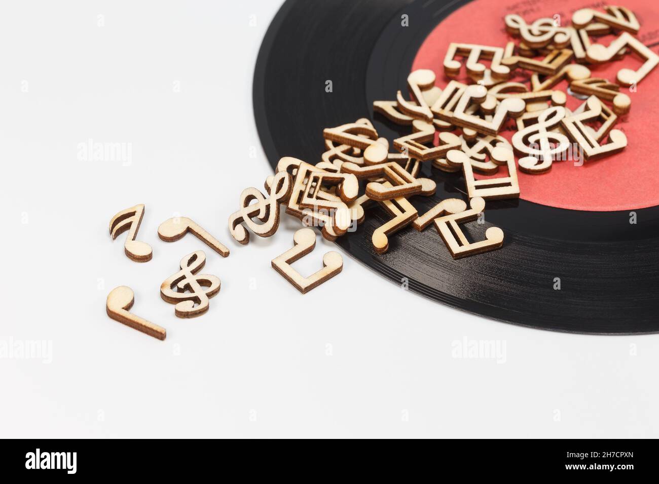 Note musicali in legno sparse su un disco in vinile, su sfondo bianco Foto Stock