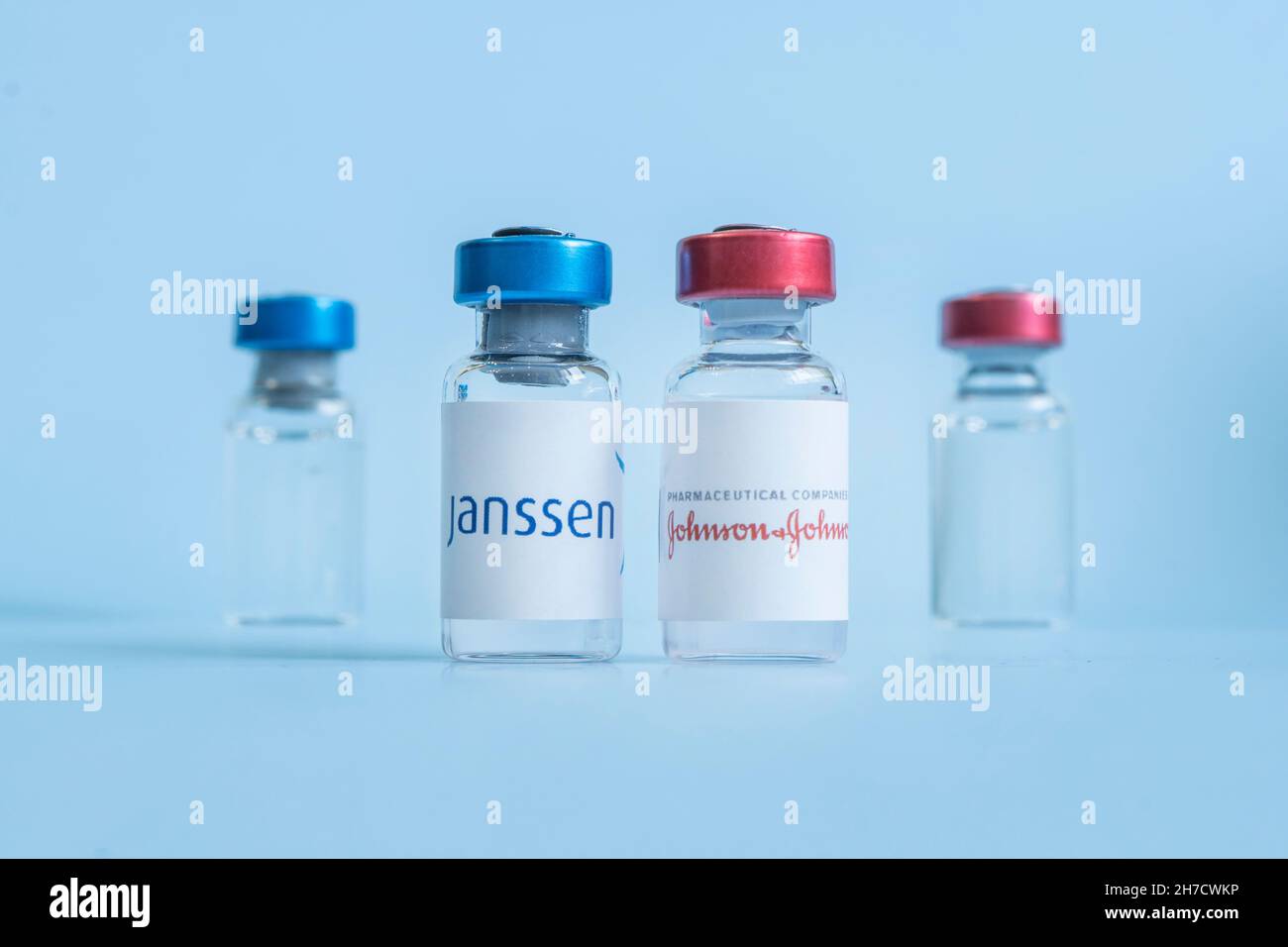 Una siringa di vaccinazione e una fiala di vetro con un liquido trasparente su sfondo blu con il logo di una società farmaceutica Johnson e Johnson. Marc Foto Stock