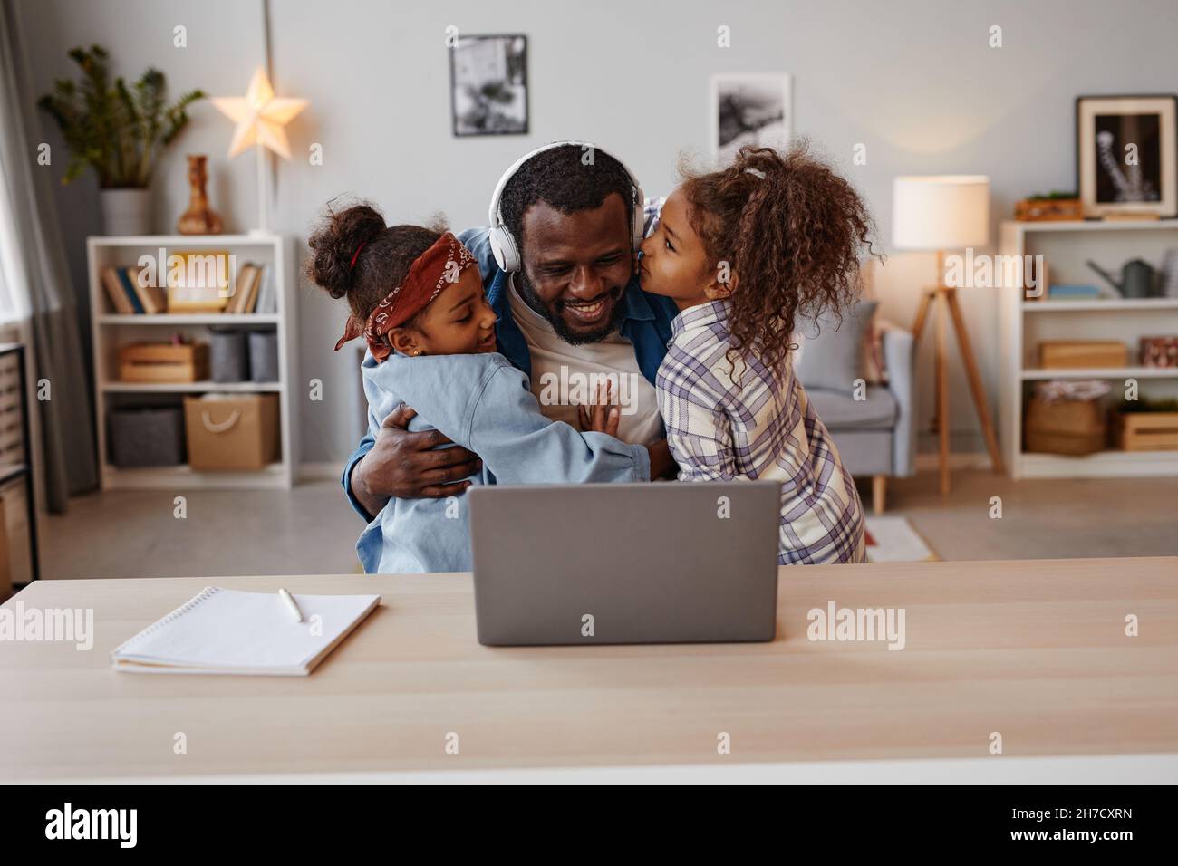 Ritratto di due bambini baciare padre afroamericano che lavora da casa, spazio copia Foto Stock