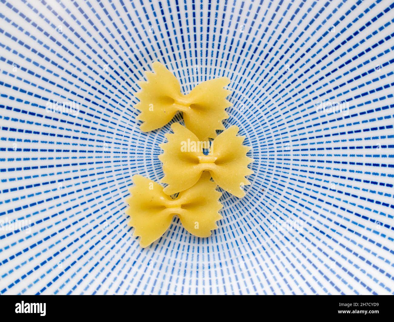 Pasta giallo chiaro a forma di farfalla su un piatto di ceramica, primo piano, vista dall'alto. Foto Stock