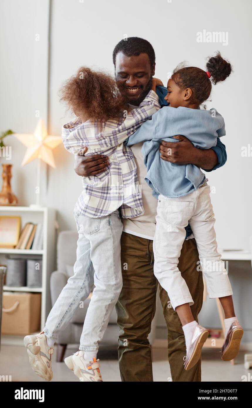 Ritratto verticale di felice padre afroamericano che tiene due simpatiche figlie a casa Foto Stock